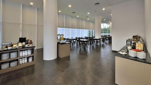 A spacious dining area with high ceilings and large windows, featuring a buffet setup with various food items and a seating area with tables and chairs. - Whiz Prime Hotel Sudirman Pekanbaru (Pekanbaru)