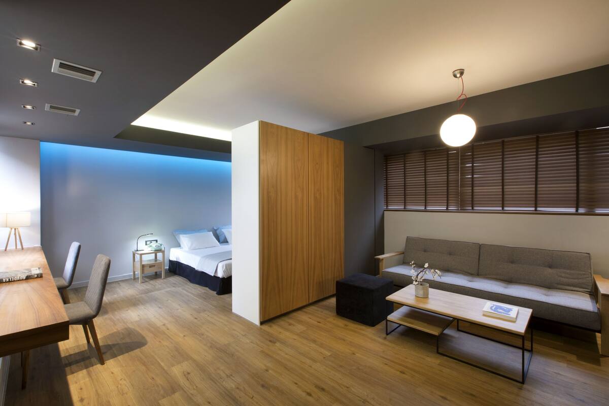 A modern hotel room with a wooden floor, a sofa, a dining table, and a bed.