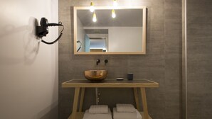 Casa de banho moderna com toucador de madeira, um espelho grande, um secador de cabelo fixado na parede e toalhas dobradas num armário.
