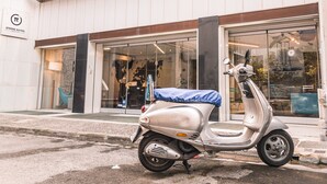 Uma scooter prateada estacionada em frente a um edifício com uma placa que diz 'ATHENS SUITES'.