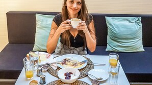 Uma pessoa sentada à mesa com itens de café da manhã, como ovos, presunto, queijo e pão.