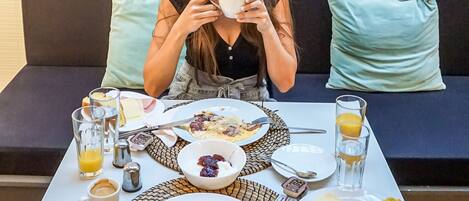 A person seated at a table with breakfast items including eggs, ham, cheese, and bread.