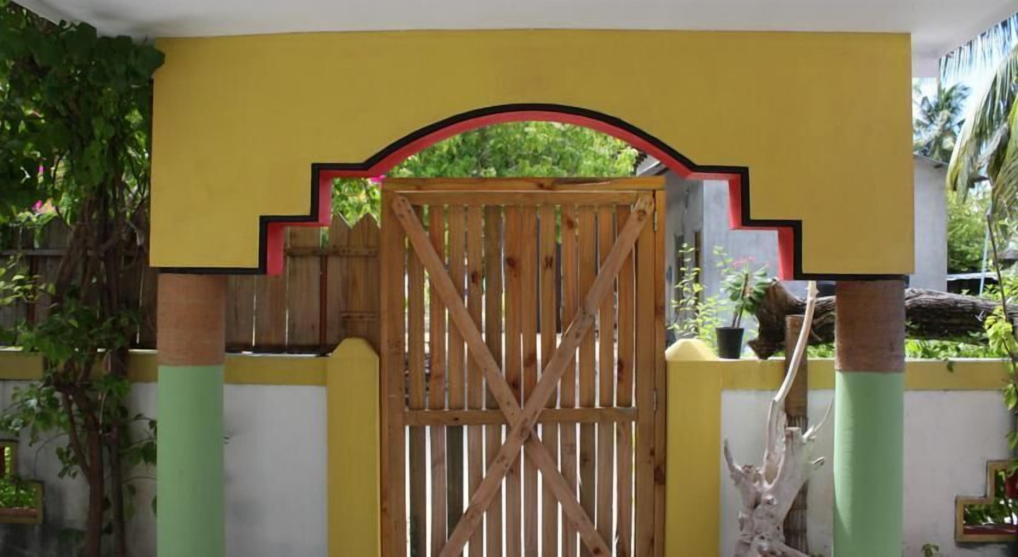 A wooden gate with a red arch, set against a yellow wall with green pillars.