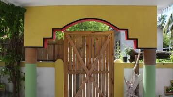 A wooden gate with a red arch, set against a yellow wall with green pillars.