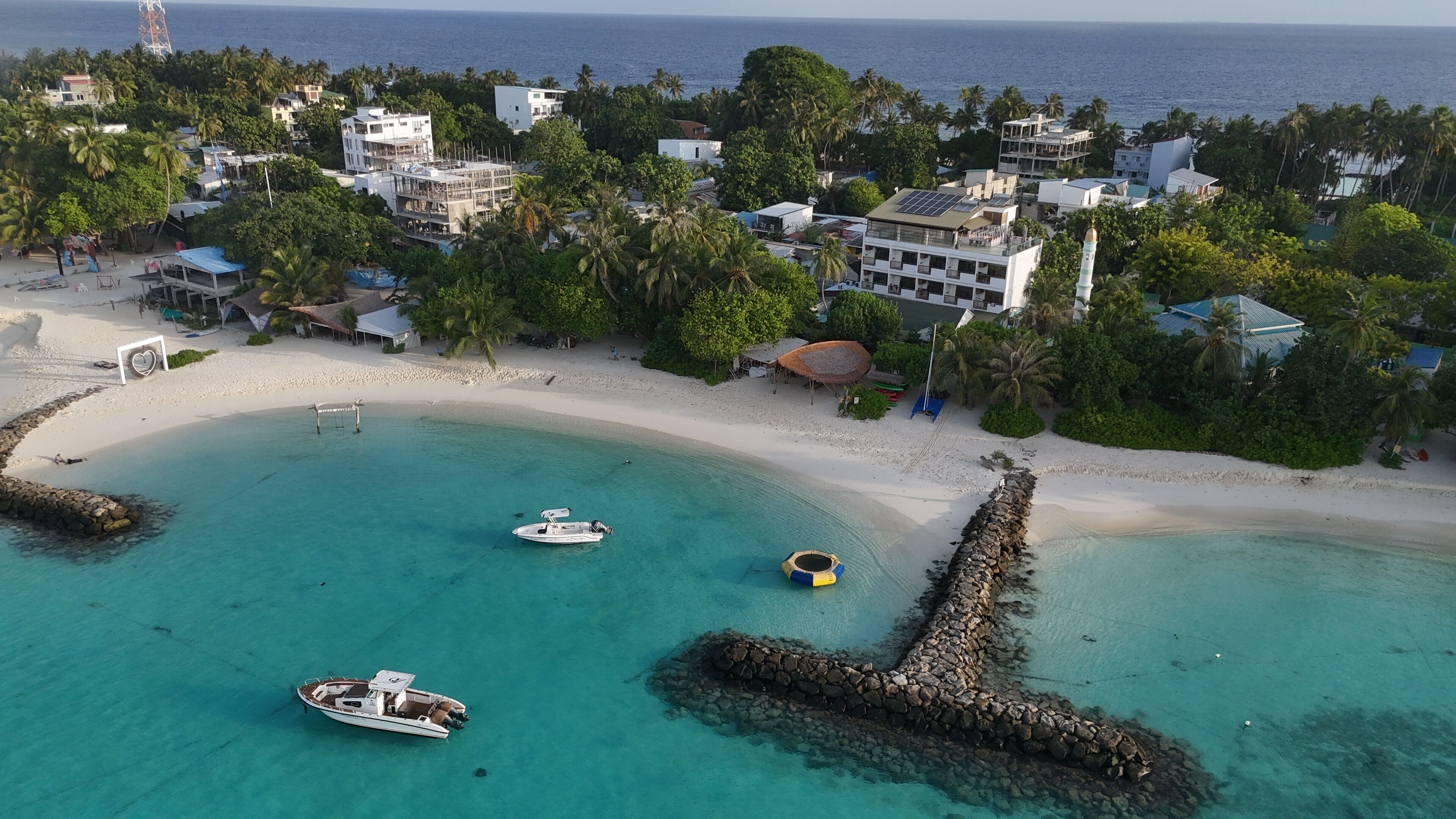 A coastal resort with a clear turquoise bay, white sandy beach, and several boats anchored near the shore.