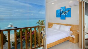 A bedroom with a wooden bed, white bedding, and a view of the ocean through a glass door. - Luau Beach Inn (Fulidhoo)