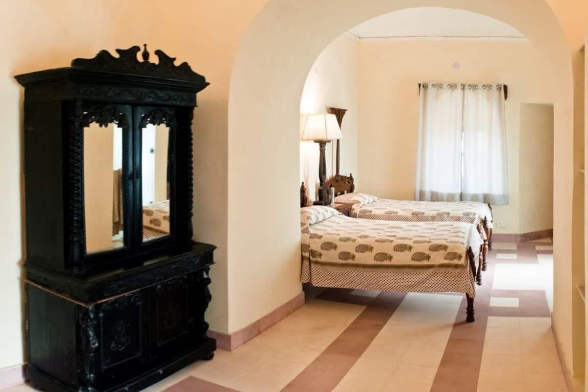 A hotel room with a large mirror, two beds with patterned bedding, a lamp, and a window with curtains.