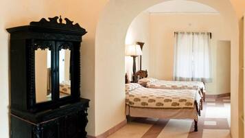 A hotel room with a large mirror, two beds with patterned bedding, a lamp, and a window with curtains.
