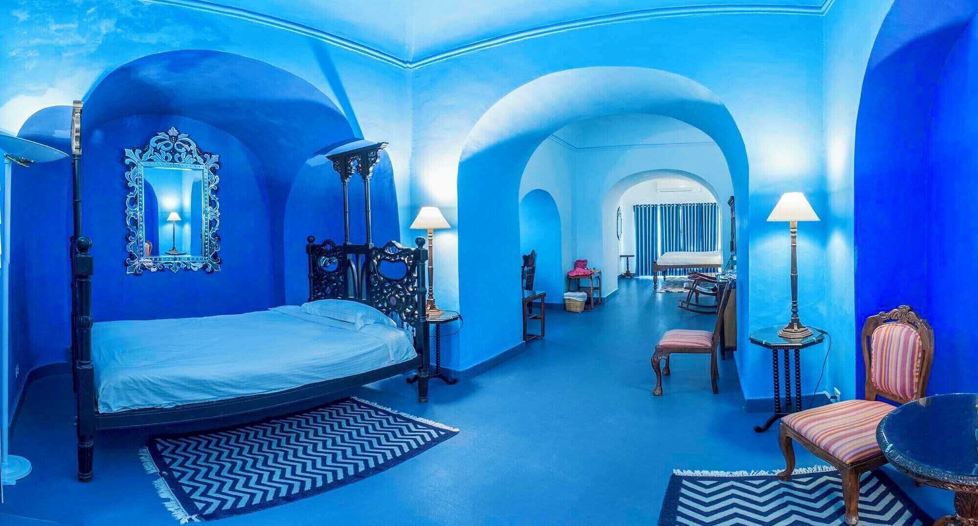 A room with a large bed, two bedside tables, a chair, a small table, and a mirror on the wall.