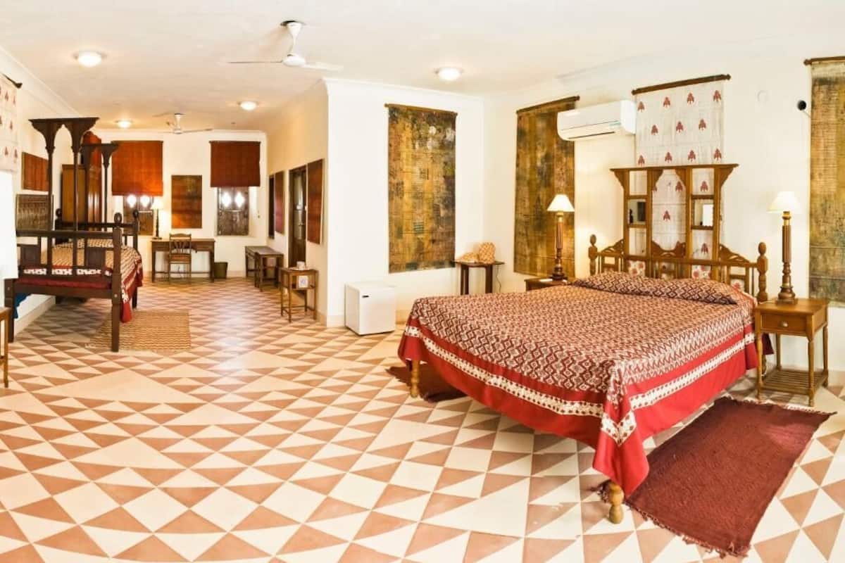 A hotel room with a checkered floor, a bed with a patterned bedspread, a wooden desk, a chair, and a wall-mounted cabinet.