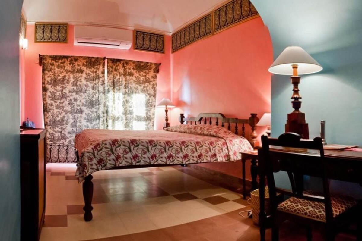 A bedroom with a bed, a desk, a chair, and a lamp.