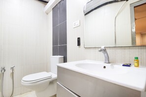 Une salle de bain avec un lavabo blanc, un miroir, des toilettes et une douche.