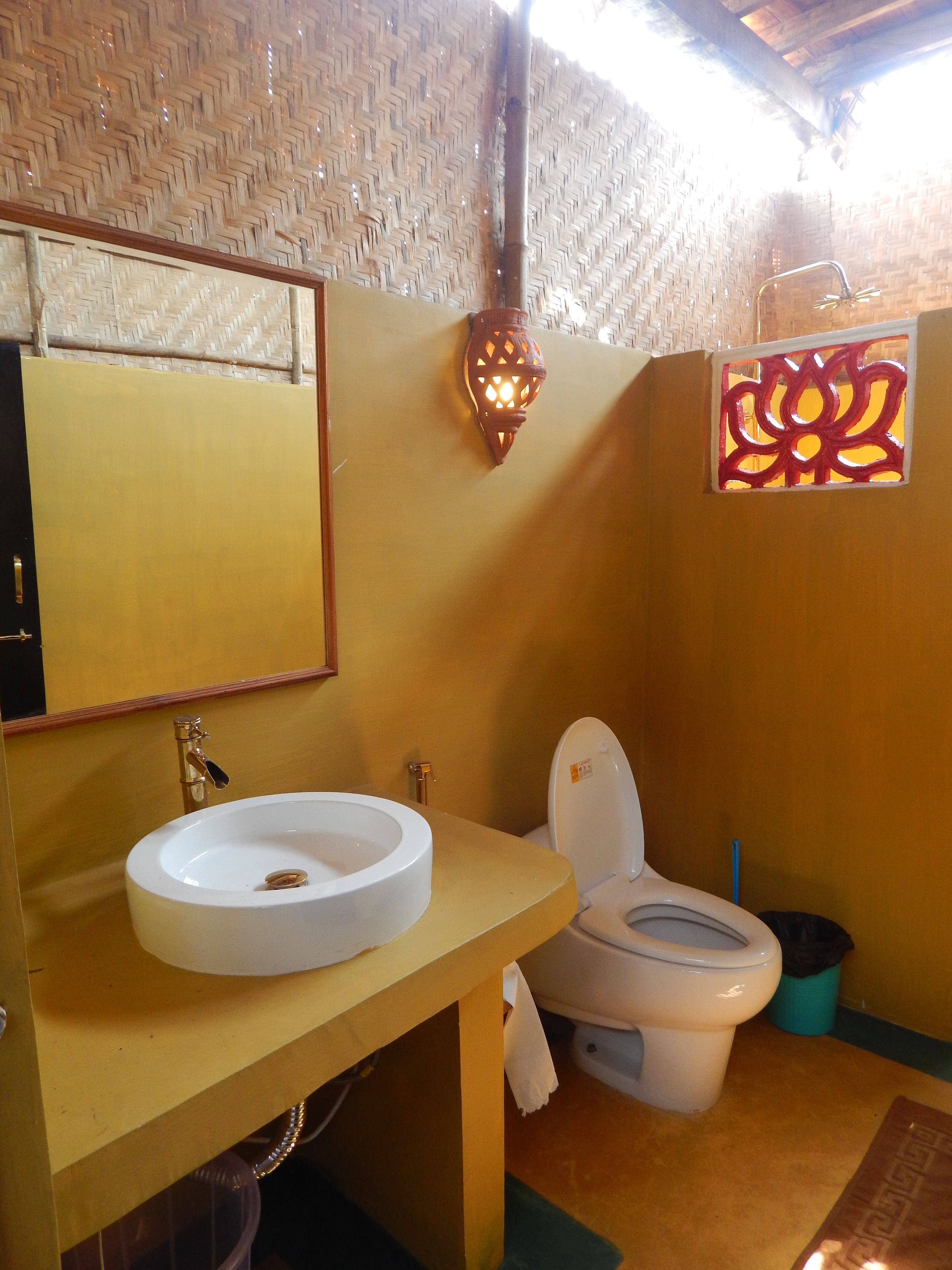 Uma casa de banho com uma pia redonda, uma sanita e um candeeiro fixado na parede.
