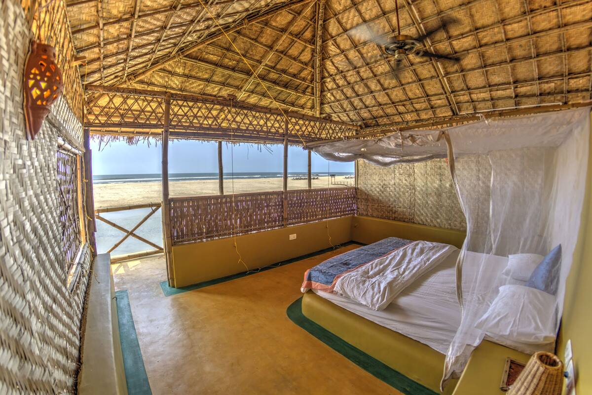 A room with a bed, a mosquito net, and a view of the beach.