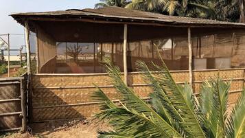 A rustic building with a thatched roof and bamboo walls, surrounded by palm trees.
