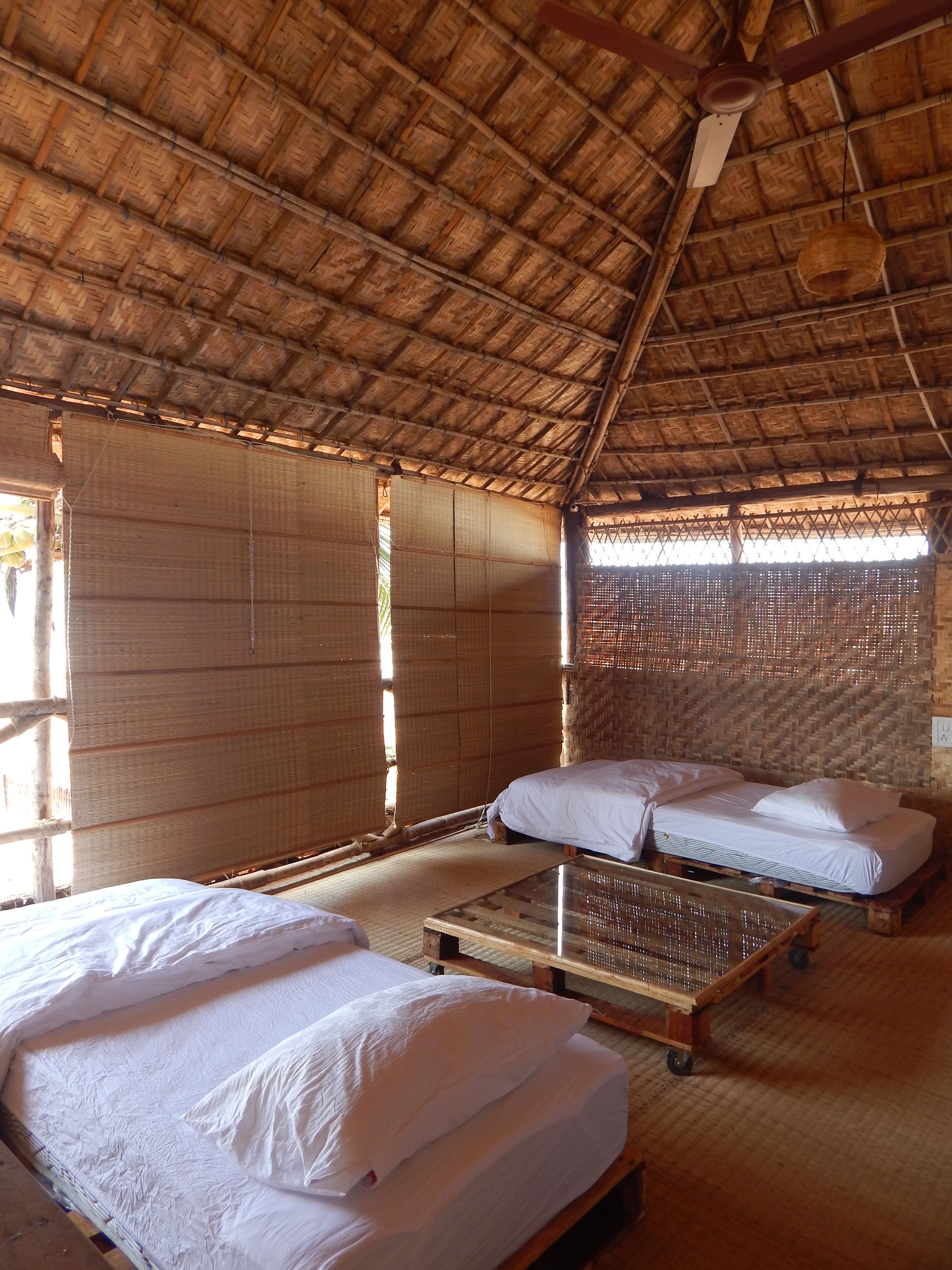 A traditional room with a thatched roof, bamboo walls, and two beds with white linens.