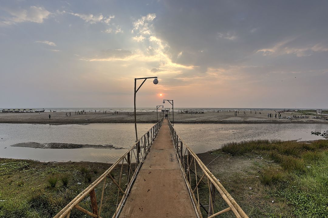 A wooden walkway leading to a beach with a sunset in the background.