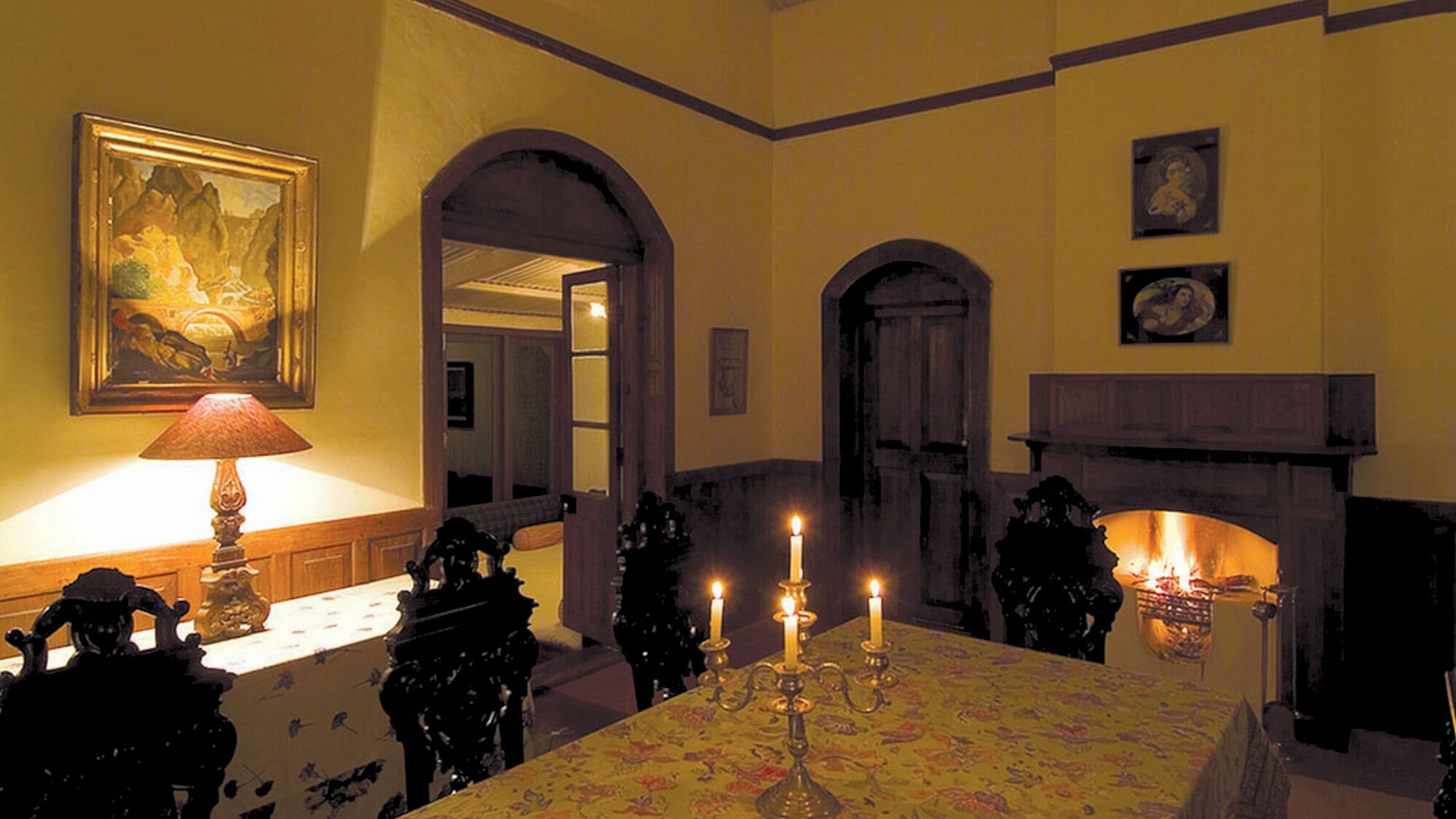 A warmly lit dining room with a table set for four, featuring a candelabra with lit candles.