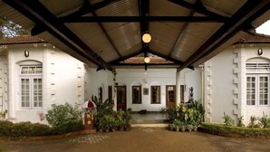 A covered entrance to a building with a central door, flanked by two smaller doors, and surrounded by potted plants.