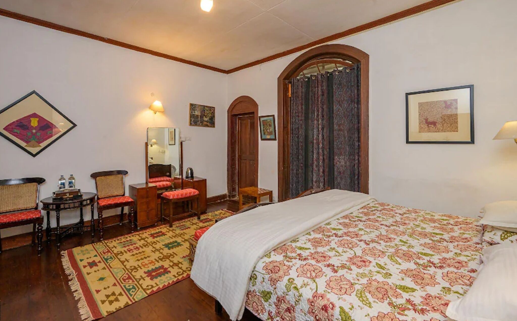 A bedroom with a bed, a desk, a chair, a mirror, and a door.
