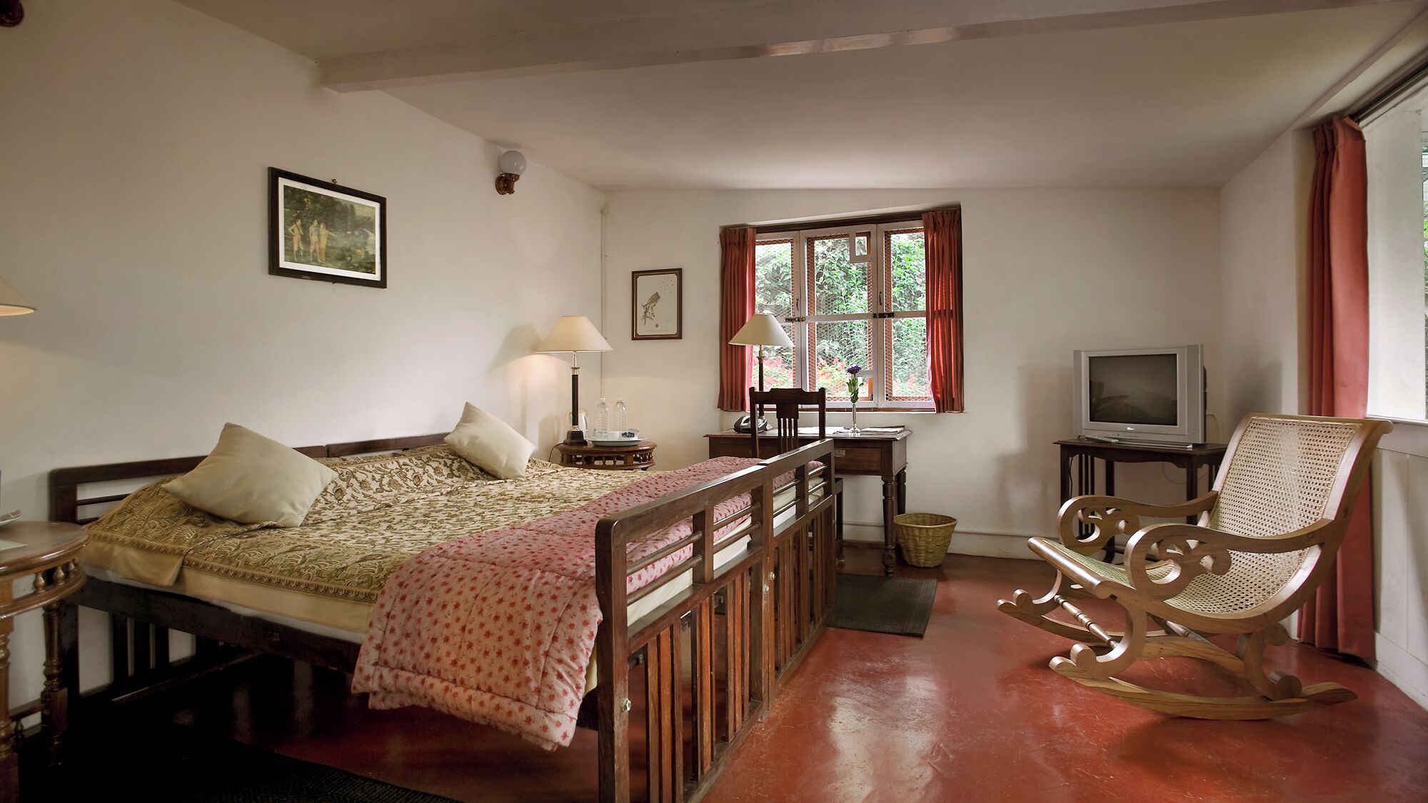 A cozy room with a bed, a desk, a rocking chair, a television, and a window with curtains.