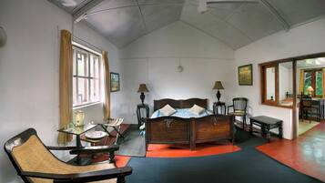 A bedroom with a wooden bed, two bedside tables with lamps, a chair, a small table with a kettle, and a window with curtains.