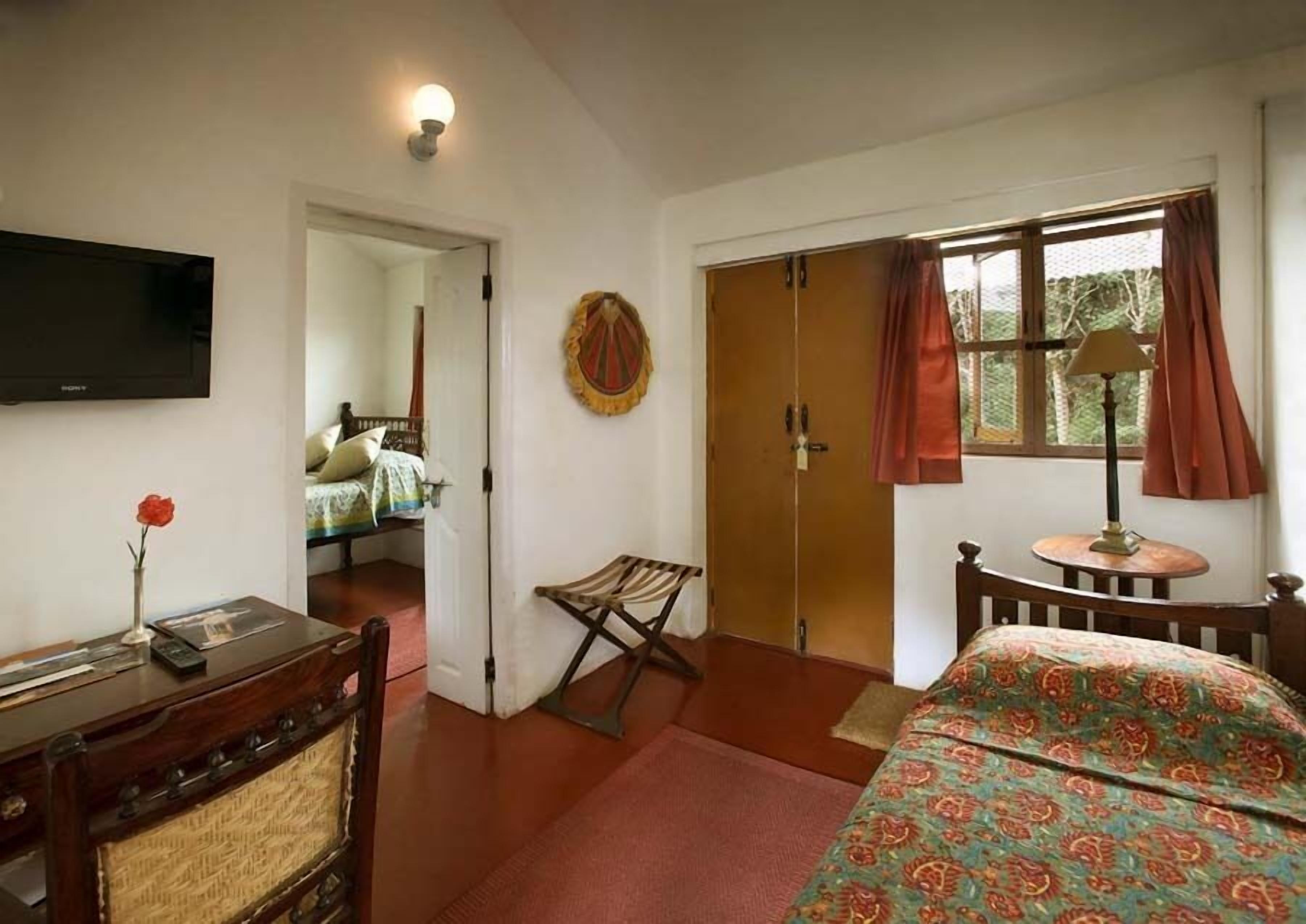 A bedroom with a bed, a desk, a TV, a wardrobe, and a window with curtains.