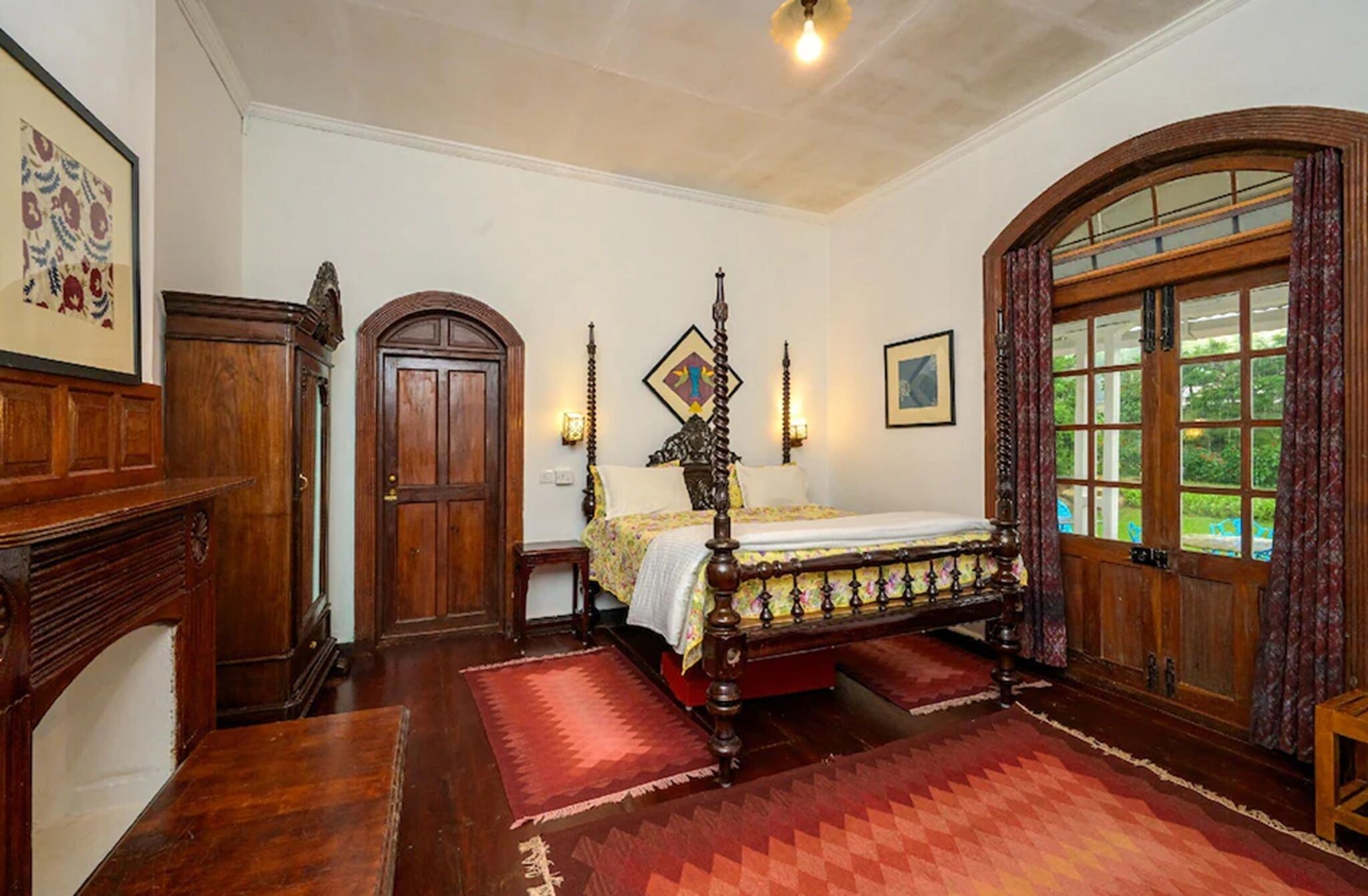 A traditional bedroom with a four-poster bed, wooden furniture, and a large window with a view.