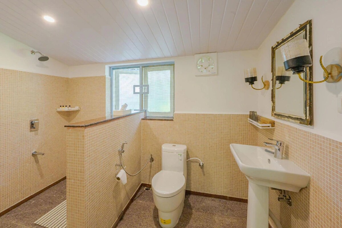 A bathroom with a toilet, sink, shower, and a window.