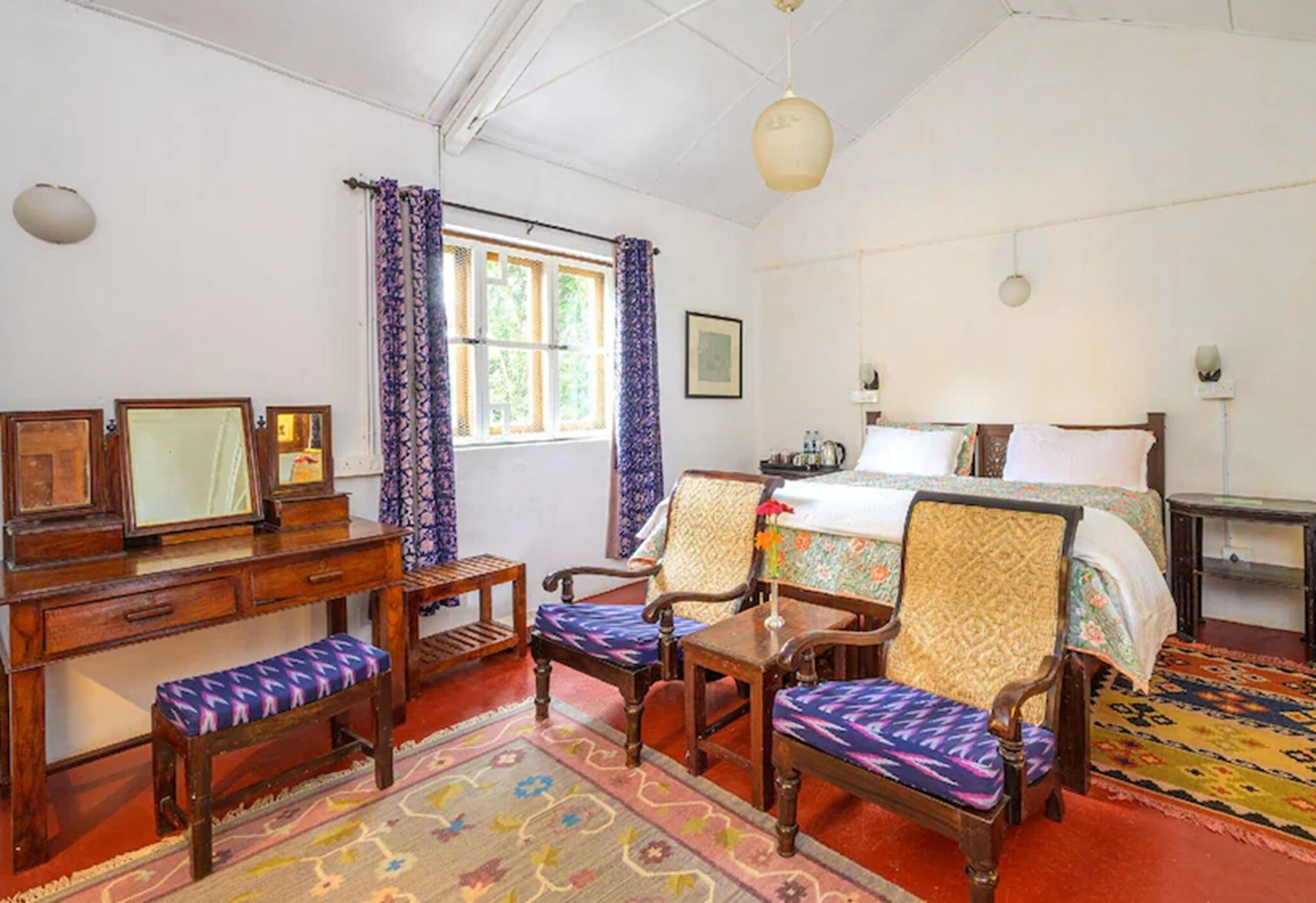 A room with a bed, a desk, a chair, a small table, and a window with curtains.