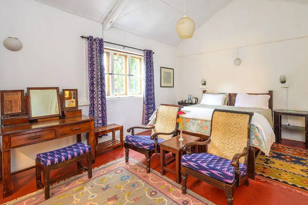Una habitación con cama, escritorio, silla, una mesita y ventana con cortinas.