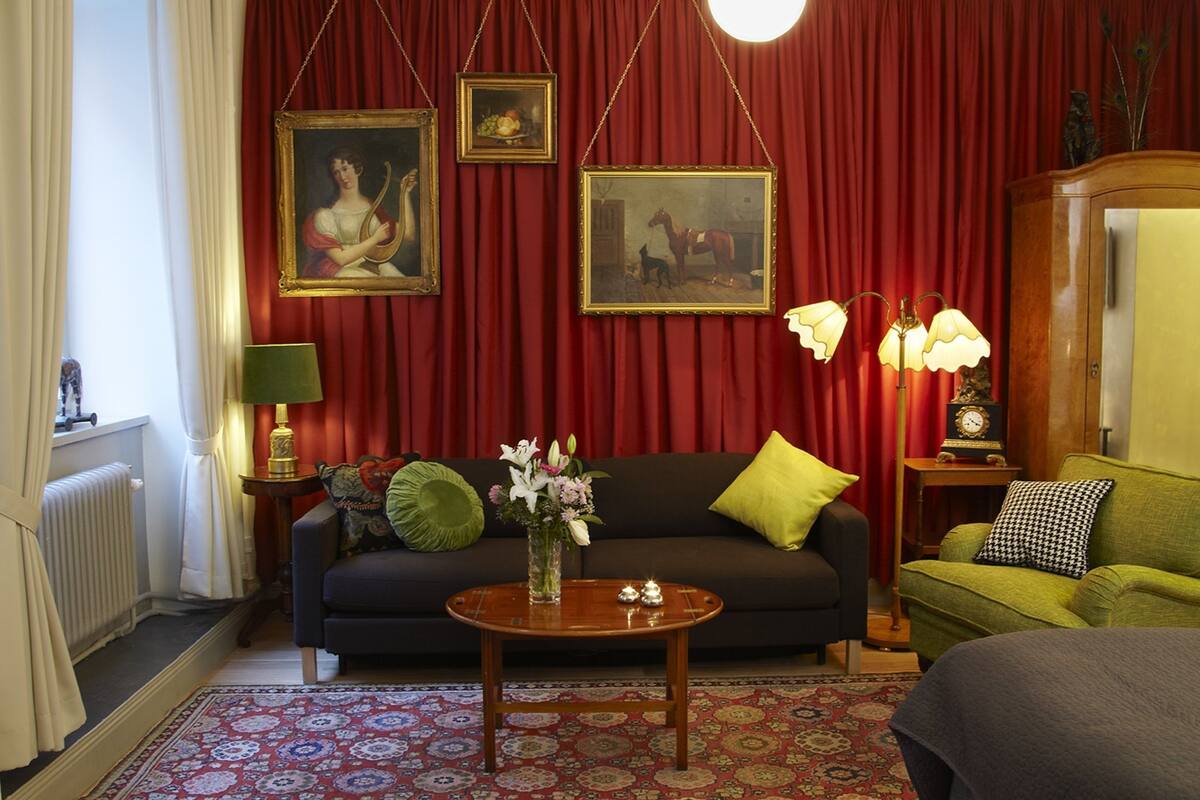 A living room with a dark sofa, a round wooden coffee table, and a red curtain backdrop.