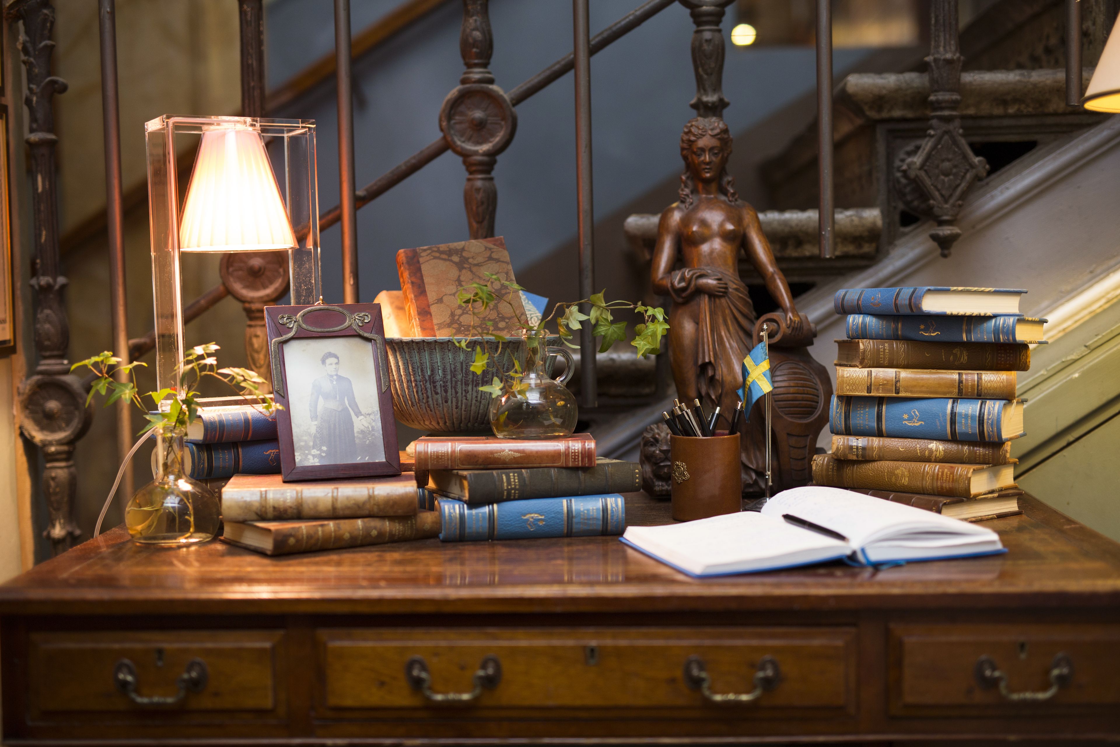 Ein Holztisch mit Büchern, einer Lampe, einer Pflanzvase, einem Bilderrahmen und einer Statue.