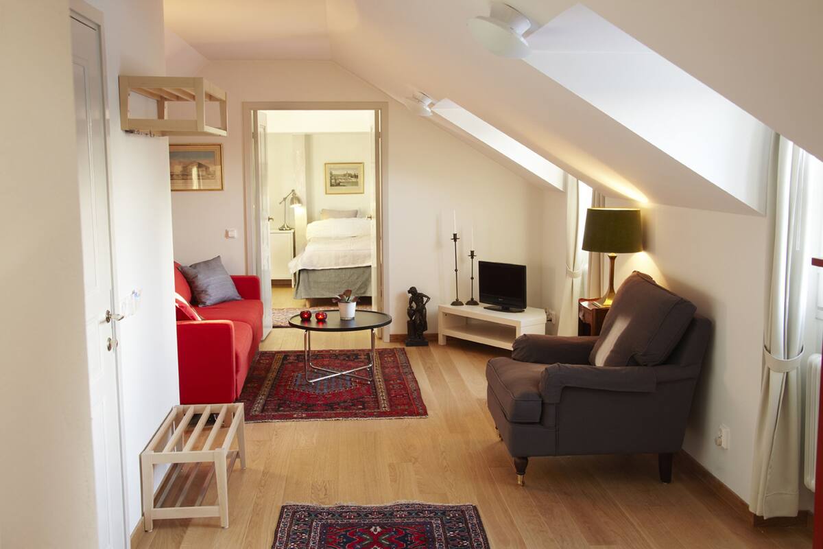 A cozy loft-style living space with a red sofa, a grey armchair, a small coffee table, and a TV.