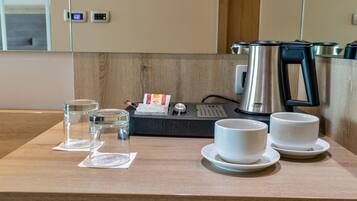 A wooden countertop with a coffee maker, two cups, and two glass containers.