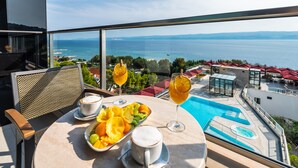 A balcony with a table set for breakfast, a swimming pool, and a view of the sea. - Hotel Plaza Duce (Dugi Rat)
