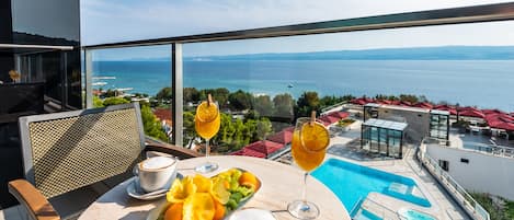 Un balcón con mesa dispuesta para el desayuno, una piscina y vistas al mar.