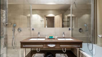 Un baño moderno con dos lavabos, un espejo y una bañera. Hay toallas y una bolsa negra en la encimera.