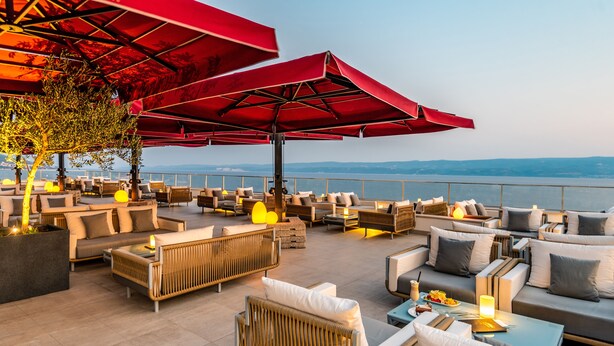 A rooftop terrace with outdoor seating, red umbrellas, and a view of the sea. - Hotel Plaza Duce (Dugi Rat)
