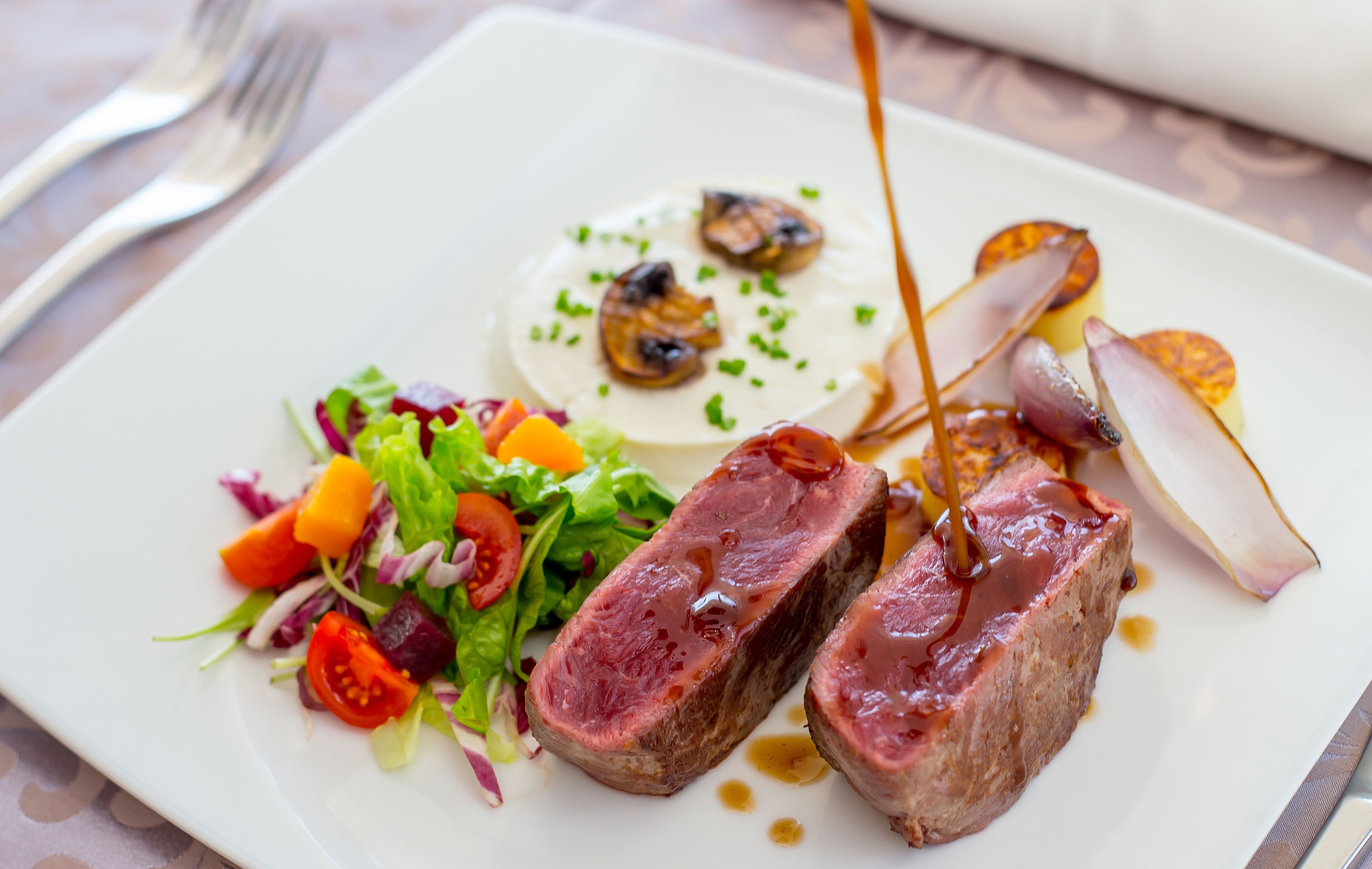 Un plato de comida con ensalada, una porción de queso y dos trozos de carne.