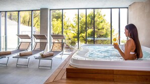 A modern indoor pool area with a hot tub, sun loungers, and large windows offering a view of trees. - Hotel Plaza Duce (Dugi Rat)