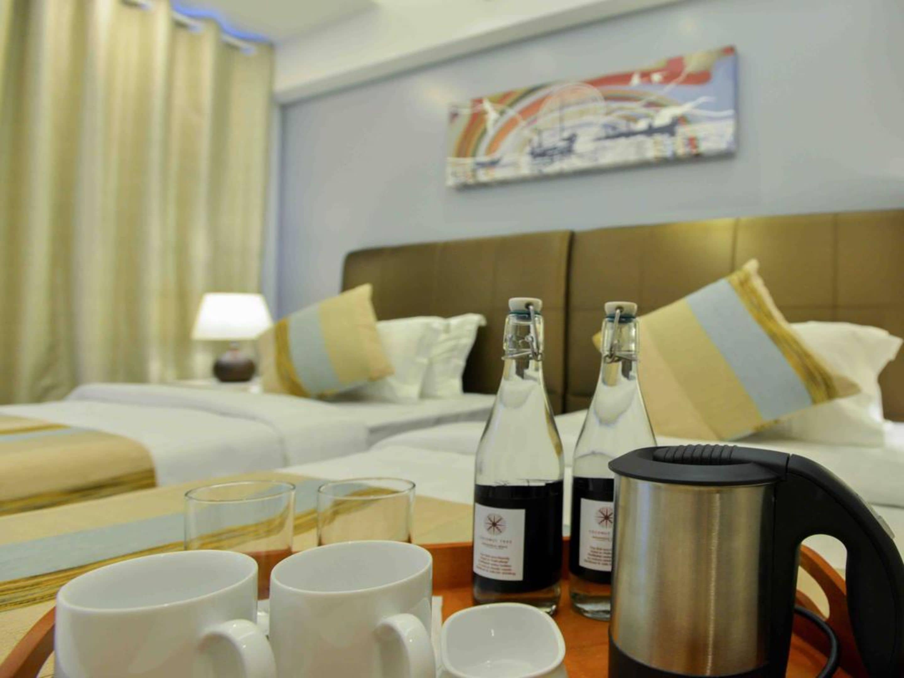 A hotel room with a bed, pillows, a coffee maker, and two bottles of water on a tray.