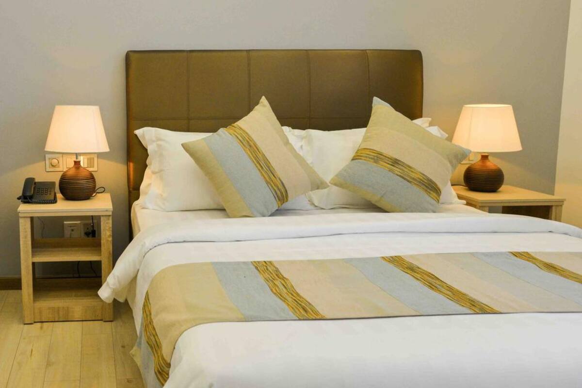 A neatly made bed with striped bedding, two bedside lamps, and a telephone on a nightstand.