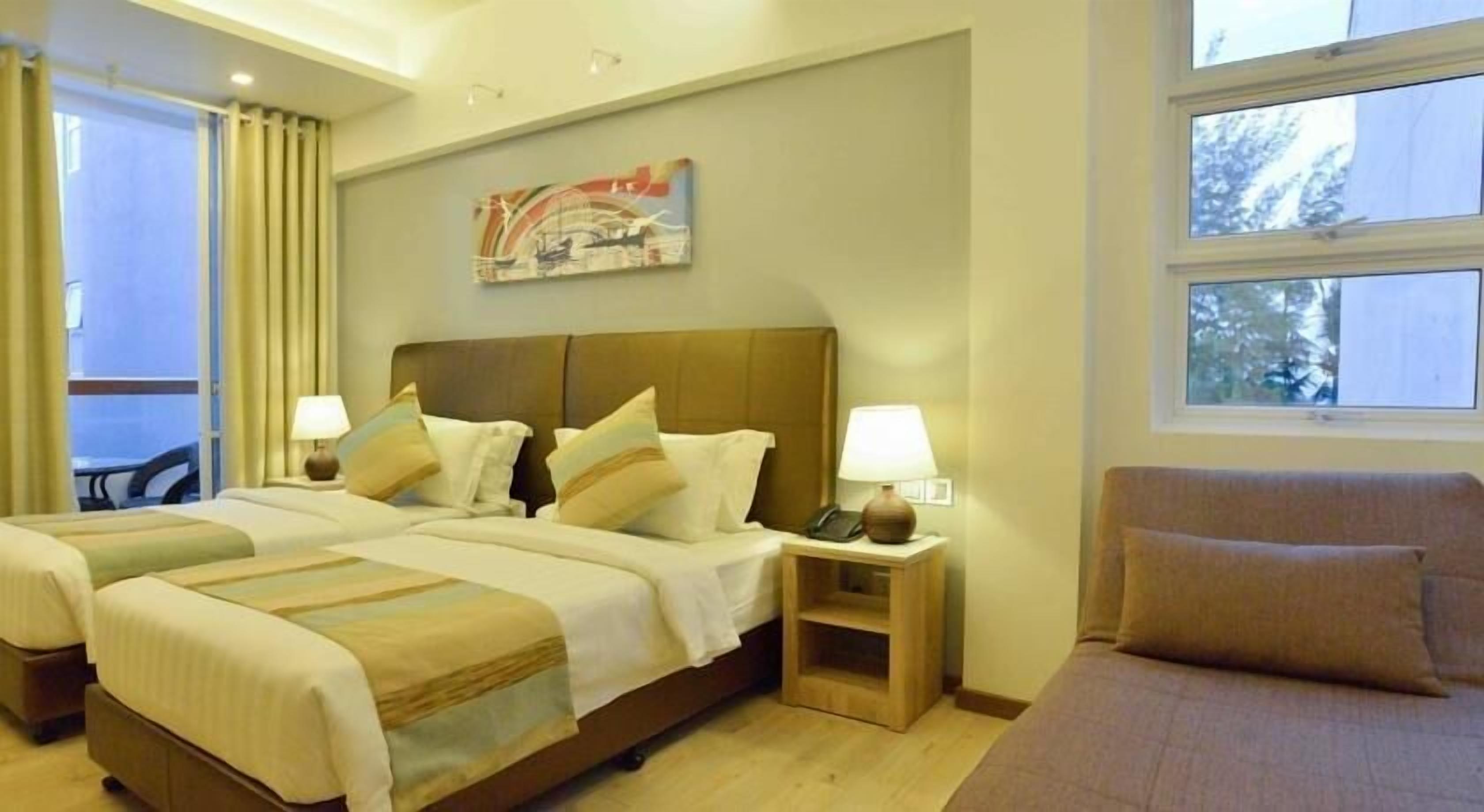A hotel room with a large bed, two bedside tables, a chair, and a window with a view of trees.