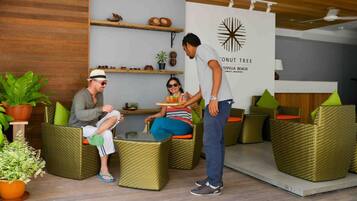 Un espacio lounge moderno con mobiliario de mimbre, un ventilador de techo y una pared con el logotipo de una palmera de coco.