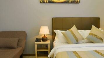 A hotel room with a bed, a nightstand with a lamp and phone, and a brown armchair.