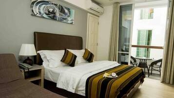 A hotel room with a bed, a desk, a chair, a lamp, and a window with curtains.