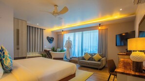 A modern hotel room with a large bed, a sofa, a desk with a lamp, a ceiling fan, and a TV. - Coconut Tree Hulhuvilla Beach (Hulhumalé)
