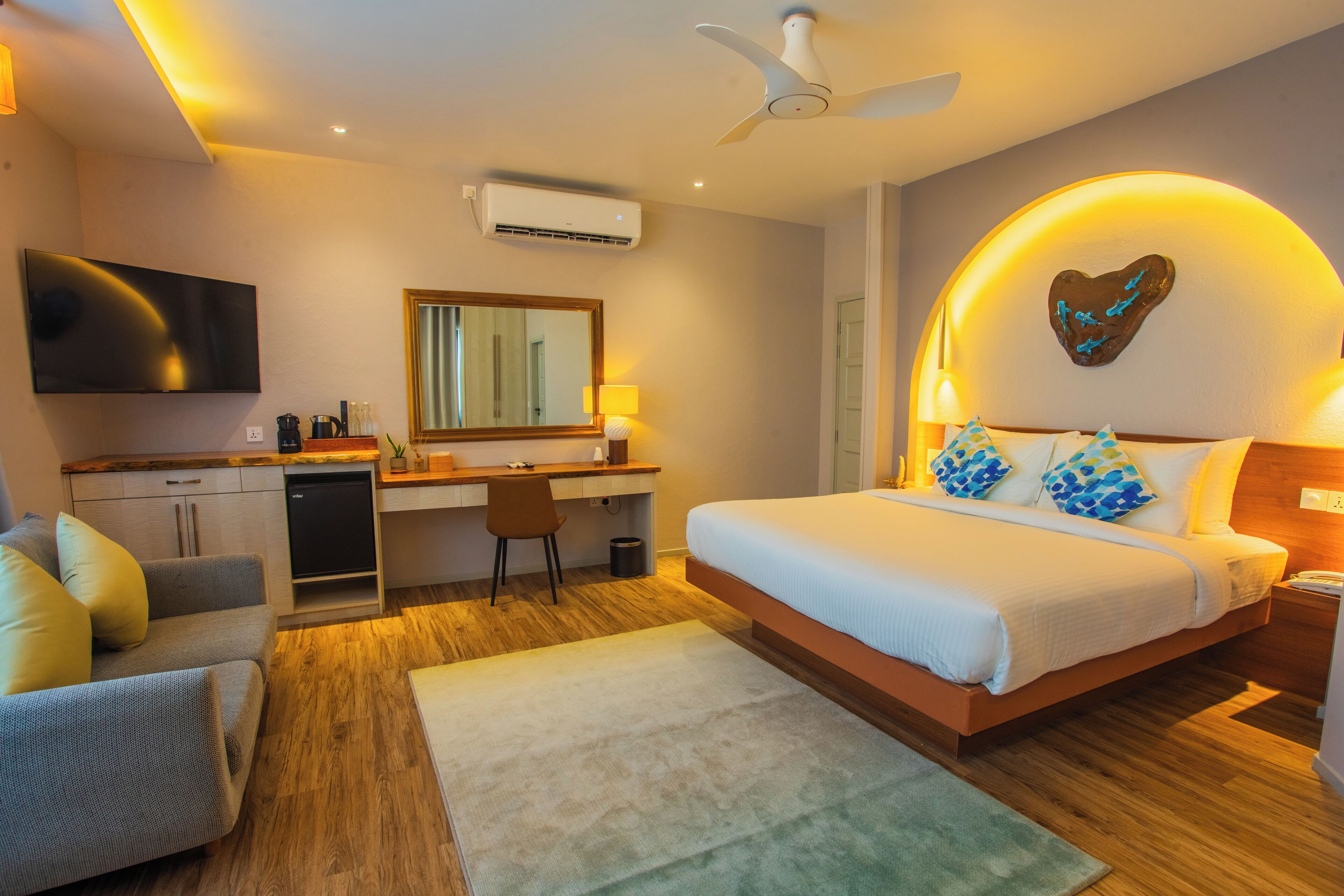 A modern bedroom with a bed, desk, and seating area, featuring a ceiling fan, air conditioning, and a heart-shaped wall decoration.