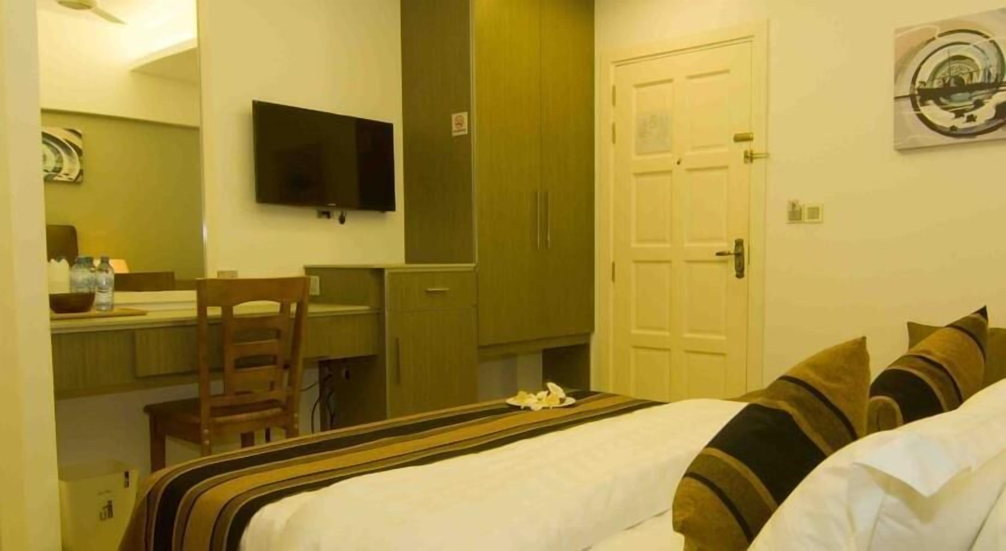 A hotel room with a bed, a desk, a chair, a television, and a wardrobe.